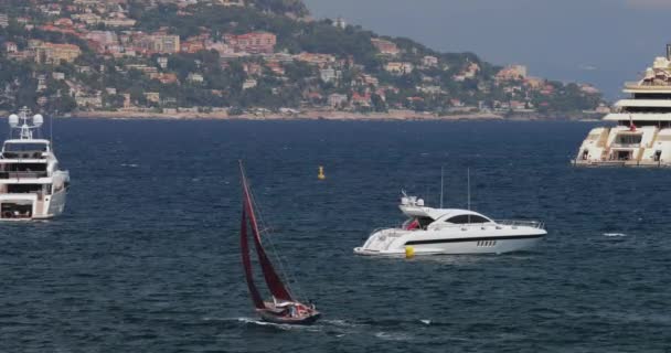 Francia, Saint-Jean-Cape-Ferrat, 29 de mayo de 2017: El barco a motor más grande del mundo Dilbar por el empresario Alisher Usmanov en el puerto, El pequeño yate de vela con una vela roja en primer plano — Vídeo de stock