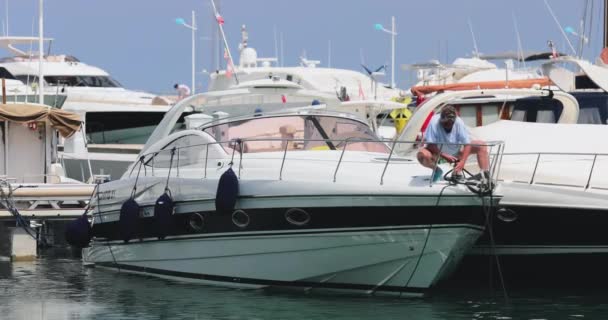 Francia, Port Saint-Jean-Cap-Ferrat, 29 maggio 2017: La coppia di anziani parcheggia lo yacht, un molo, megayachts sullo sfondo, tempo soleggiato — Video Stock