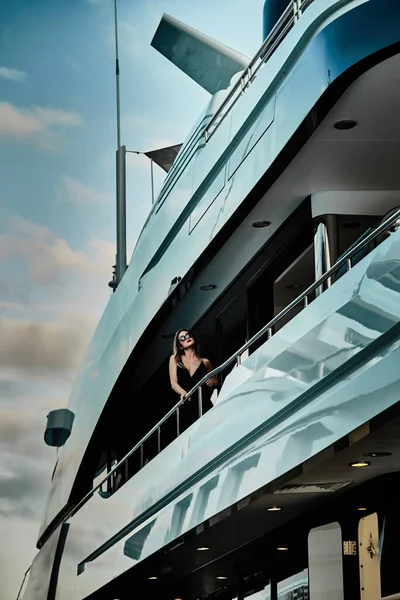 Una diva glamorosa en un vestido de noche de color negro y gafas de sol se encuentra en la cubierta superior de un enorme yate en anticipación — Foto de Stock