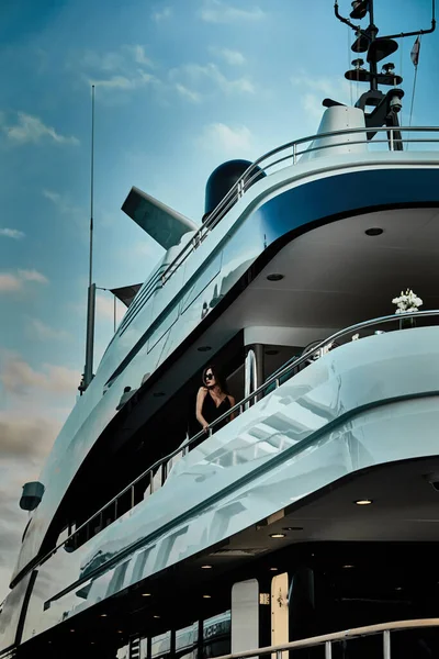 Egy elbűvölő díva áll egy fekete színű estélyi ruhában és napszemüvegben egy hatalmas jacht fedélzetén várakozva. — Stock Fotó