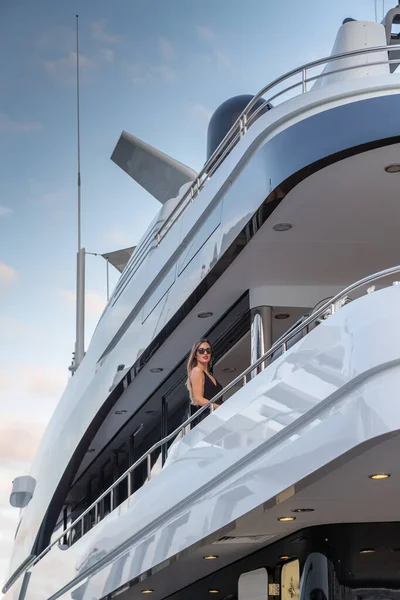 Элегантная девушка одета в вечернее платье черного цвета и солнцезащитные очки стоит на верхней палубе огромной яхты в ожидании, красные губы, великолепная леди, она делает волосы — стоковое фото