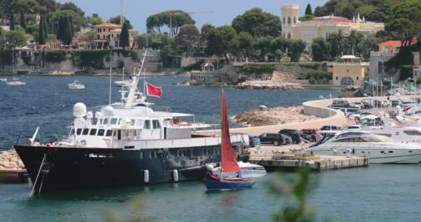 Francia, Saint-Jean-Cap-Ferrat, 29 maggio 2017: Il faro nel porto, mega yacht all'orizzonte, acqua azzurra, un sacco di barche da pesca e yacht, un molo, spiaggia di Paloma — Video Stock