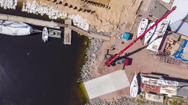 Russia, St.Petersburg, 26 May 2020: Time-lapse of the big industrial crane lifts the sailboat and floats it, the beginning of a season of sailing, a skyscraper on a background, drone view point — Stock Video