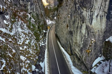 Kayalık dağ ormanlarındaki bir yılanın insansız hava aracı görüntüsü, Bicaz vadisi kış mevsiminde dolambaçlı yol ile, Cheile Bicazului, Romanya