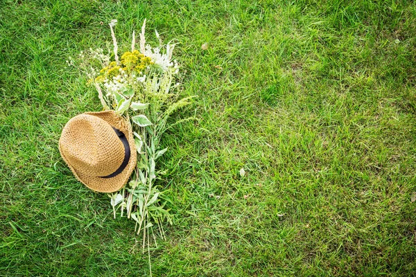 Chapeau de paille et bouquet de fleurs sauvages sur pelouse verte — Photo