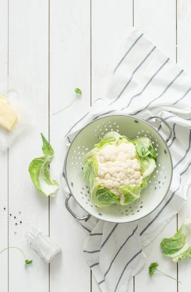 Coliflor fresca cruda húmeda en un colador sobre madera rústica blanca — Foto de Stock