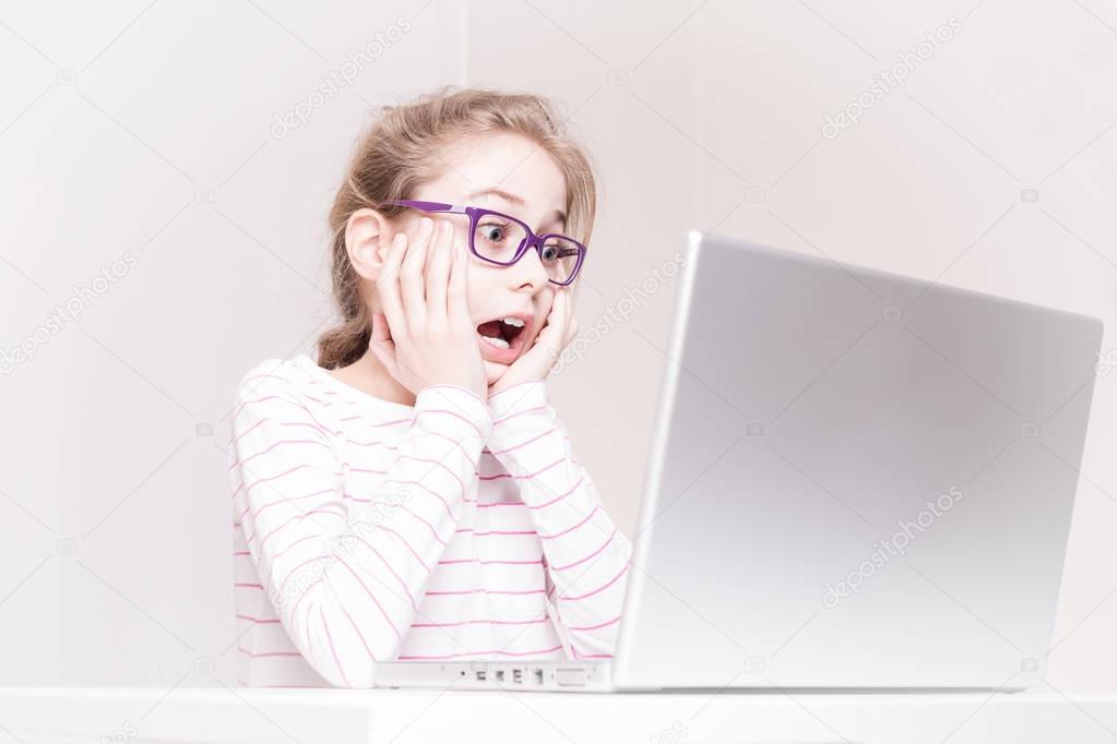 Surprised and shocked child girl (kid) using laptop computer