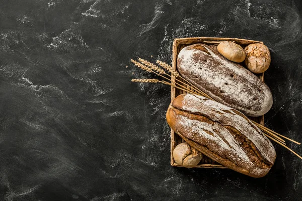 Bakery - rustic crusty loaves of bread and buns on black — Stock Photo, Image