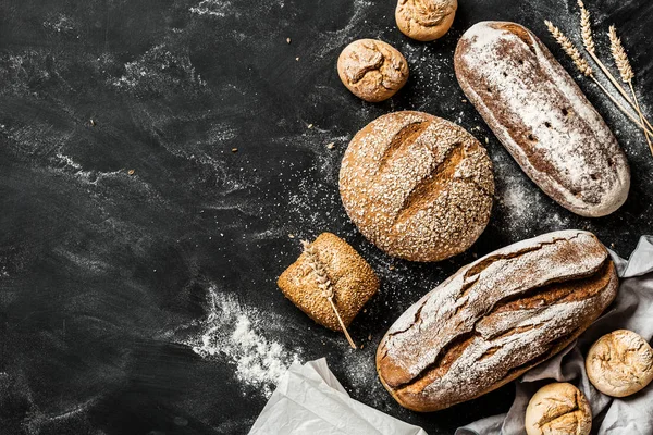 Bakery - rustic crusty loaves of bread and buns on black — Stock Photo, Image