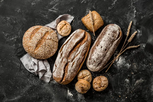 Bakery - rustic crusty loaves of bread and buns on black — Stock Photo, Image