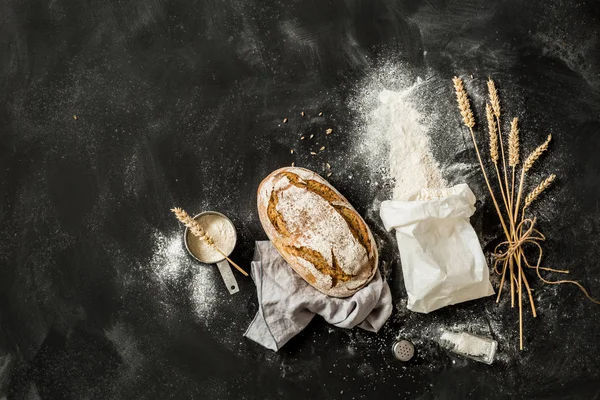 Pão, saco de farinha, trigo e xícara de medição em preto — Fotografia de Stock