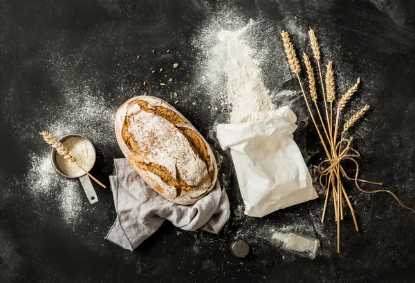 Bread, flour bag, wheat and measuring cup on black