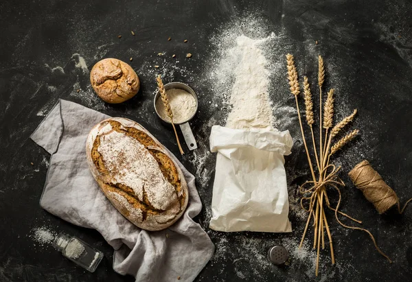 Pain, sac de farine, blé et tasse à mesurer sur noir — Photo