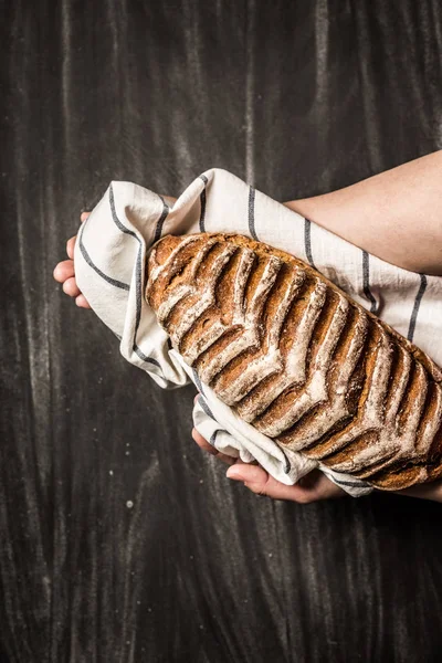 Rustykalne chrupiący bochenek chleba w baker's ręce na czarny — Zdjęcie stockowe