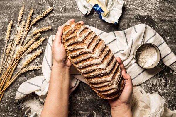 Pão crocante rústico nas mãos do padeiro em preto — Fotografia de Stock