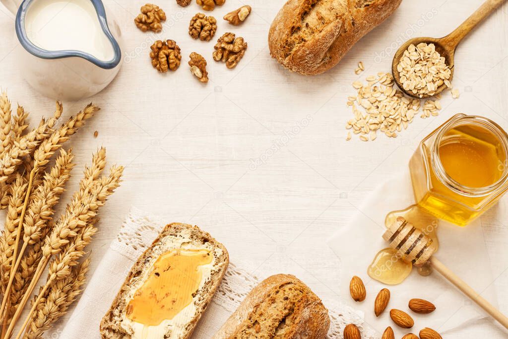 Rural or country breakfast - bread rolls, honey jar, milk, nuts and wheat on white wood from above. Background layout with free text space.