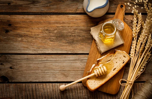 Honey in a jar, slice of bread, wheat and milk on an old vintage planked wood table from above. Rural or rustic style breakfast concept. Background layout with free text space.