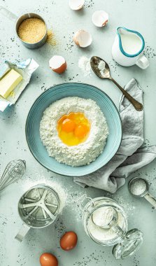 Mutfak - hamur hazırlama. Un ve yumurtalı kase. Pastel mavi taş arka planda temel gıda malzemeleri (tereyağı, süt, şeker) bulunur. Yukarıdan yakalanmış (üst görünüm, düz uzanma).