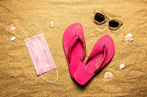 外科用フェイスマスク ピンクのフリップフロップと砂の上のサングラス 夏休み コロナウイルス中 Covid 流行の概念 上からのビーチ 上からの眺め フラットレイアウト — ストック写真