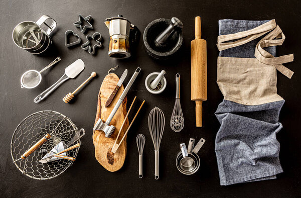 Kitchen utensils (cooking tools) and chef's apron on black chalkboard background. Kitchenware collection captured from above (top view, flat lay).