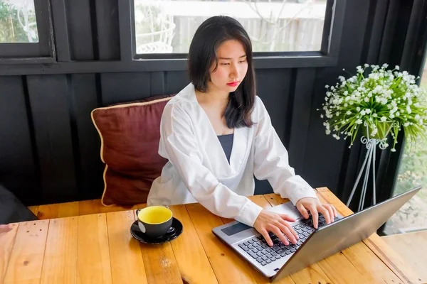 Beyaz gömlekli bir Asyalı kız defter siyah odasında ahşap masa üzerinde çalış.