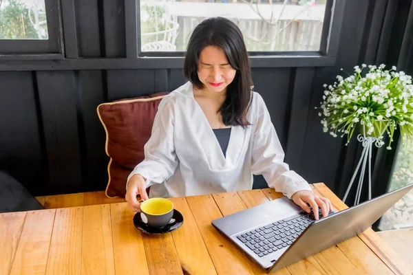 Beyaz gömlekli bir Asyalı kız defter siyah odasında ahşap masa üzerinde çalış.