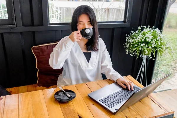 Beyaz gömlekli bir Asyalı kız defter siyah odasında ahşap masa üzerinde çalış.