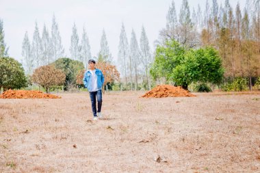 Tayland 'da kuru bir ormanda tek başına duran beyaz günlük ve kot ceketli Asyalı bir çocuk..