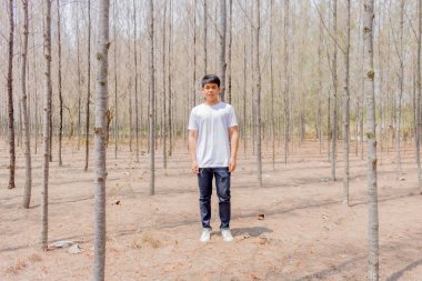 Tayland 'ın kuru ormanlarında beyaz pantalonlu Asyalı bir çocuk tek başına dikiliyor..