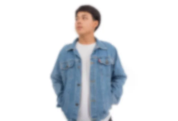 Bulanık bir fotoğrafta siyah saçlı Asyalı bir çocuk beyaz gömlek ve kot ceketle stüdyoda tek başına duruyor..