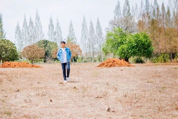 Tayland 'da kuru bir ormanda tek başına duran beyaz günlük ve kot ceketli Asyalı bir çocuk..