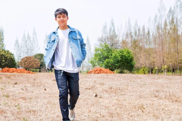 一名身穿白色休闲装和牛仔裤夹克的亚洲男孩独自站在泰国干燥的森林里 — 图库照片
