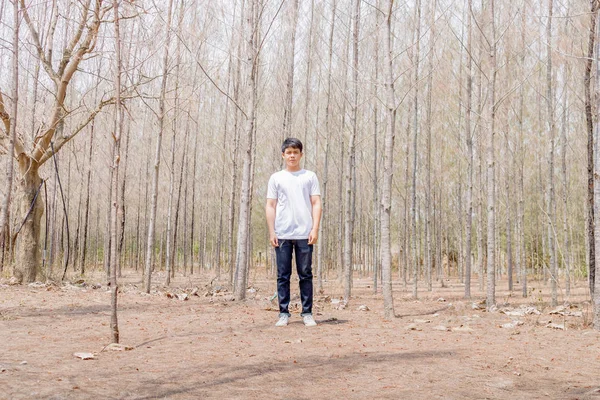 Tayland 'ın kuru ormanlarında beyaz pantalonlu Asyalı bir çocuk tek başına dikiliyor..