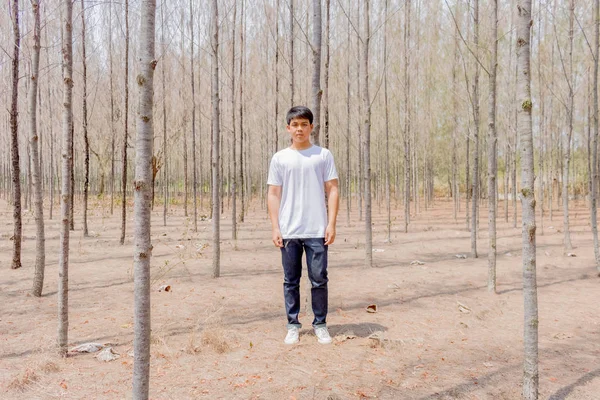 Tayland 'ın kuru ormanlarında beyaz pantalonlu Asyalı bir çocuk tek başına dikiliyor..