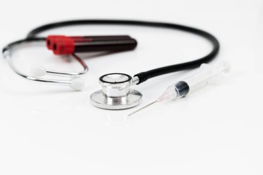 Tıbbi ekipman şırınga, kan örneği içeren plastik test tüpü ve beyaz arka planda izole edilmiş steteskop ve seçici odaklanma içerir.