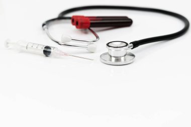 Tıbbi ekipman şırınga, kan örneği içeren plastik test tüpü ve beyaz arka planda izole edilmiş steteskop ve seçici odaklanma içerir.