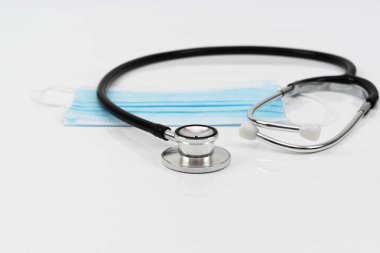 Tıbbi yüz maskesi ve steteskop beyaz arka planda izole edilmiş ve seçici odaklanma