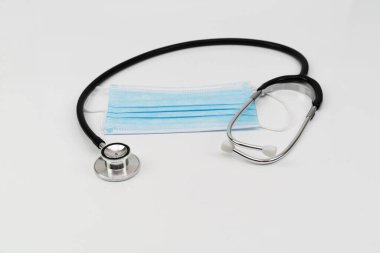 Tıbbi yüz maskesi ve steteskop beyaz arka planda izole edilmiş ve seçici odaklanma
