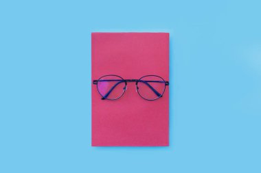 Gözlükler pembe kitaba yerleştirilmiş, mavi arka plana yerleştirilmiş, Üst Manzara