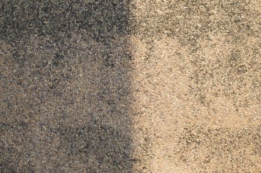 Beton zemin, eski ve lekeli, çatının gölgesine bölünmüş..