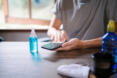 Coronavirus koruma konsepti, akıllı telefonu alkolle temizlemek, yakın plan....