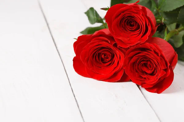 Three red roses lie on white table — Stock Photo, Image