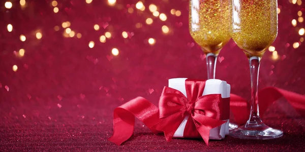 Zwei Gläser Champagner mit verpacktem Geschenk lila Glitzerhintergrund — Stockfoto