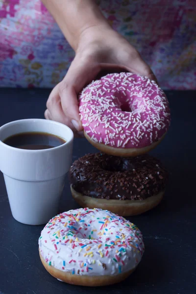 Coffee and hand holding donut on a black background — Stock Photo, Image