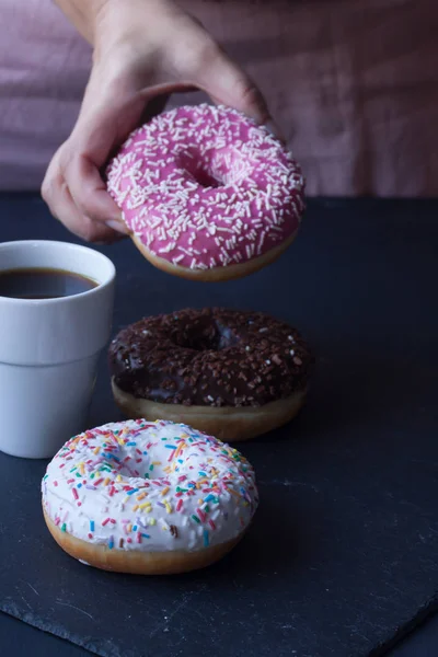 Coffee and hand holding donut on a black background — Stock Photo, Image