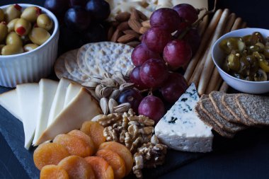 peynir, üzüm, kraker ve siyah bir zemin üzerine zeytin