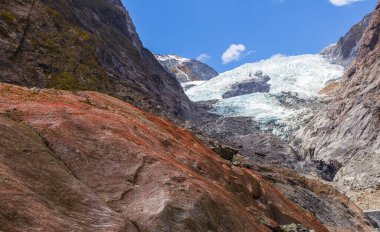 Buzulun arka planındaki kırmızı kaya parçası. Franz Joseph Buzulu, Yeni Zelanda