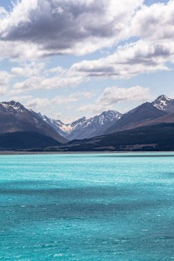 Pukaki Gölü. Turkuaz suyu olan bir gölün üzerindeki mavi dağlar. Güney Alpleri. Yeni Zelanda