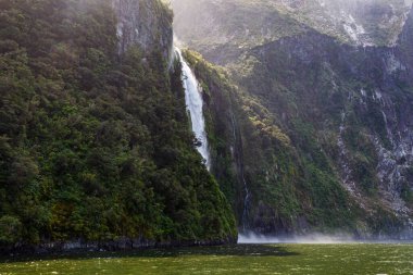 Küçük bir şelale ve yeşilliklerle kaplı bir dağ manzarası. İtfaiyeciler Ulusal Parkı. Güney Adası, Yeni Zelanda