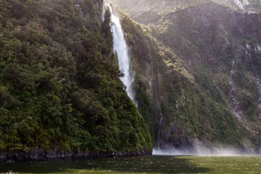 Küçük bir şelale ve yeşil bir dağ manzarası. İtfaiyeciler Ulusal Parkı. Güney Adası, Yeni Zelanda
